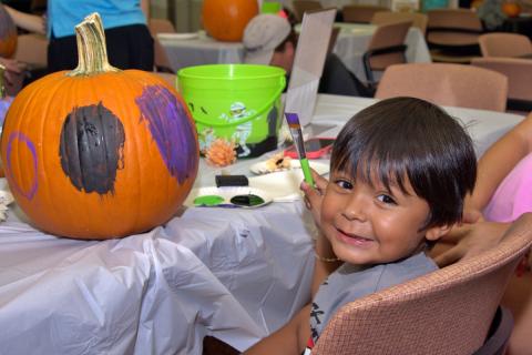 Child smiles while painting a pumpkin